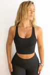 Front view of model posing in the fitted stretchy cropped black flexrib Varsity Tank Bra with a scoop neckline
