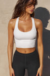 Front view of model posing in the fitted stretchy cropped white  flexrib Varsity Tank Bra with a scoop neckline