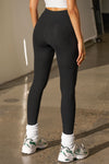 Back view of model from the waist down posing in the sleek and stretchy full length sueded onyx The Body Legging with a mid-rise elastic waistband