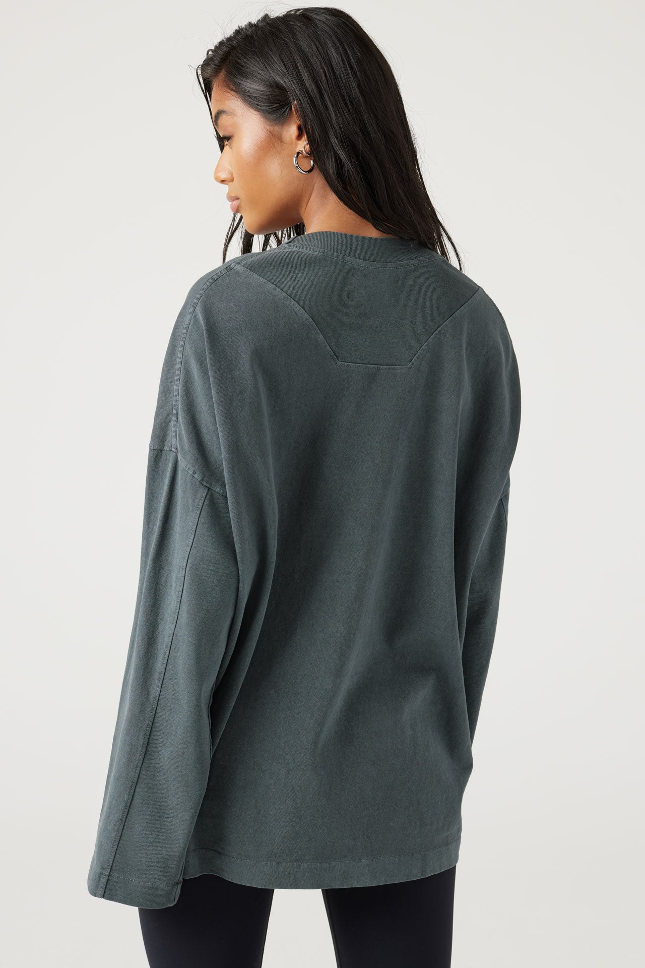Back view of model posing in oversized evergreen cotton Vintage Long Sleeve top with a crew neckline and ribbed accents at the upper back