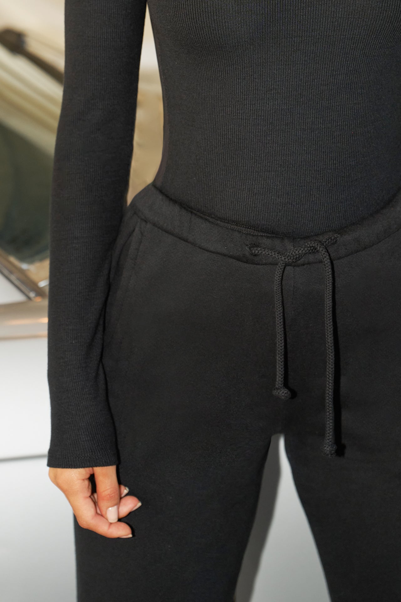 Close up detail front view of model from the waist down posing in the tapered black french terry Empire Jogger with side pockets and an elastic waistband and ankle cuffs
