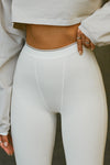 Close up detail front view of model from the waist down posing in the stretchy high-waisted bone flexrib Essential Legging with boxer-style stitching, cuffed ankles and an elastic waistband