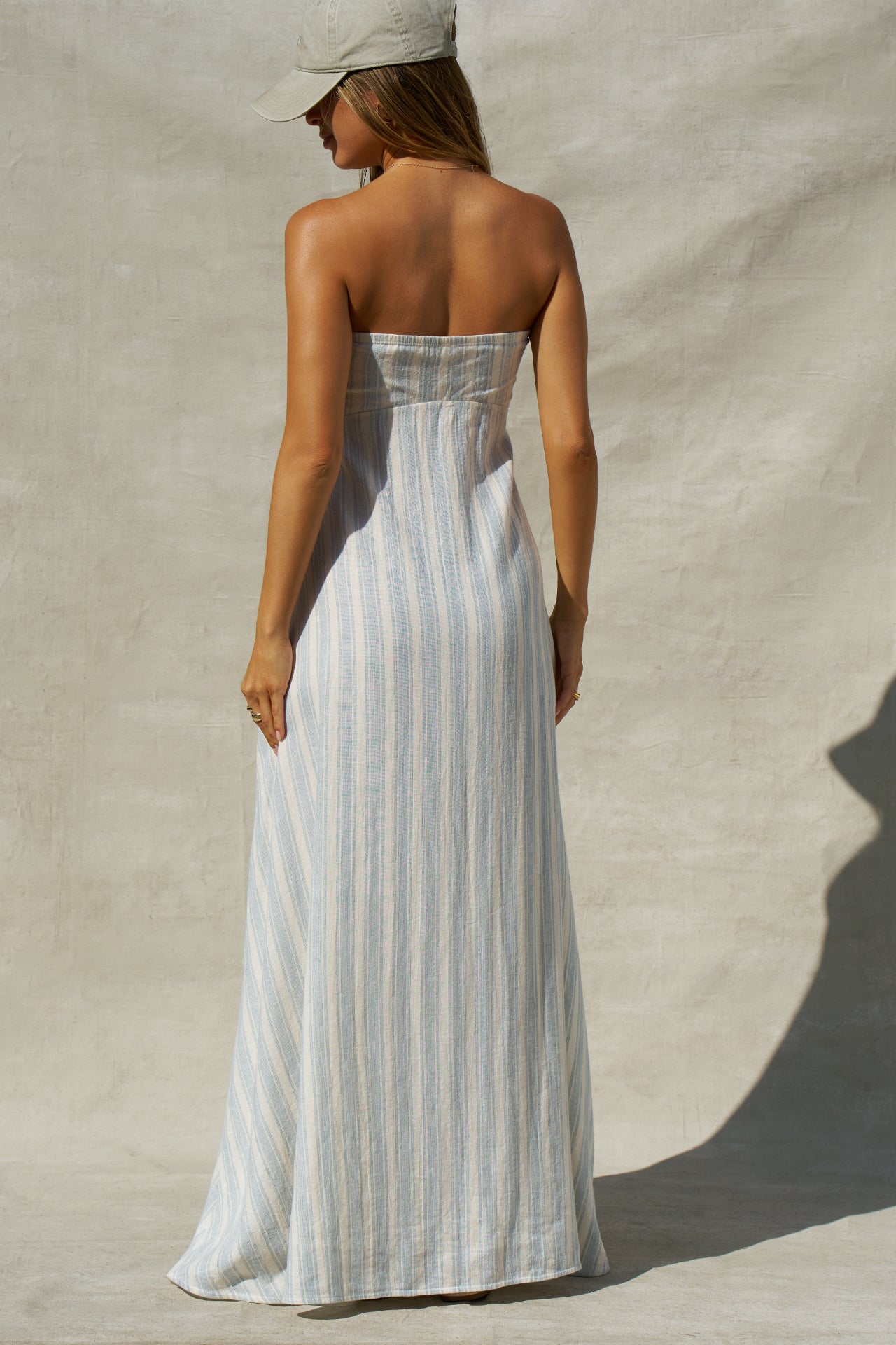 Back view of model posing in the relaxed-fit lightweight natural white and blue stripe gauze Essential Maxi Dress with a straight neckline, fitted bodice and removable adjustable straps 