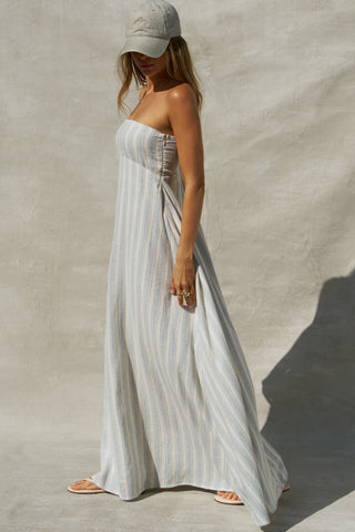 Side view of model posing in the relaxed-fit lightweight natural white and blue stripe gauze Essential Maxi Dress with a straight neckline, fitted bodice and removable adjustable straps 