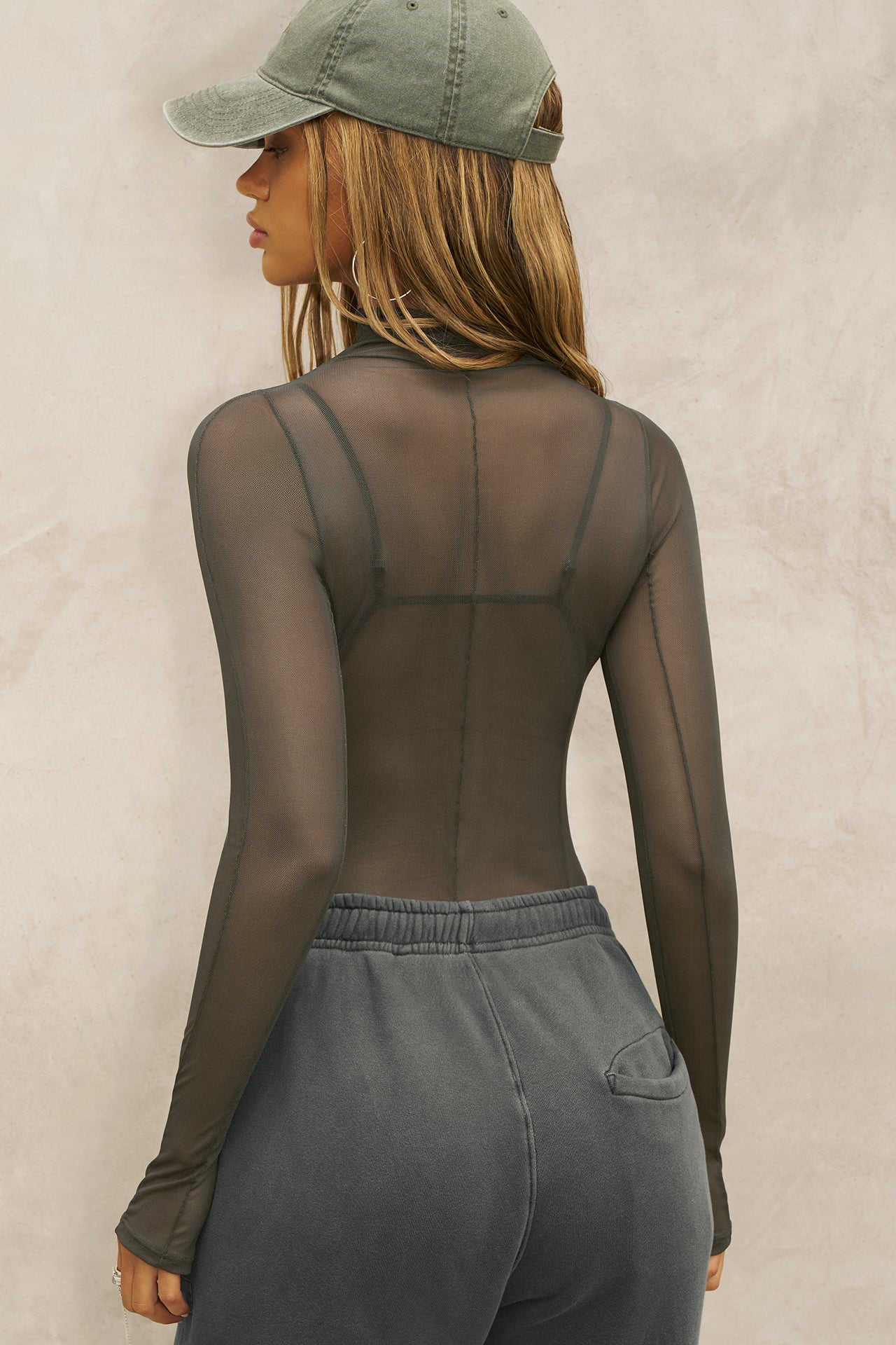 Back view of model posing in the fitted and sheer graphite mesh Exposed Seams Long Sleeve top with a mock neckline and exposed seam details
