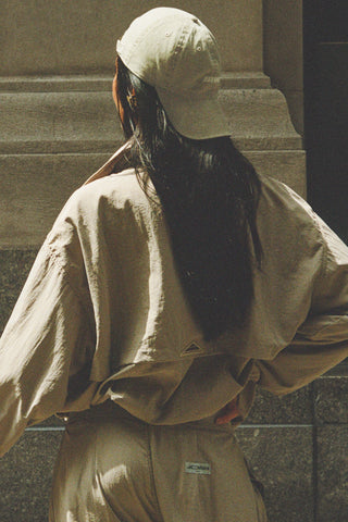 Back view of model wearing the six-panel desert Official Cap with a curved brim and an embroidered upside down Joah Brown logo on the front backwards on her head