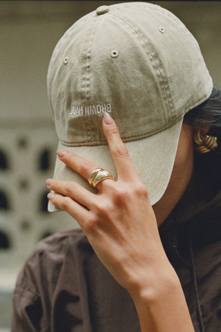 Close up side view of model wearing the six-panel desert Official Cap with a curved brim and an embroidered upside down Joah Brown logo on the front