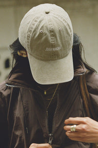 Close up front view of model wearing the six-panel desert Official Cap with a curved brim and an embroidered upside down Joah Brown logo on the front