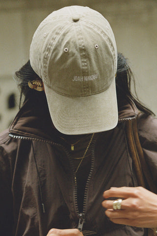 Close up front view of model wearing the six-panel desert Official Cap with a curved brim and an embroidered upside down Joah Brown logo on the front