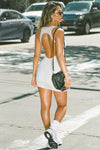 Full body back view of model posing in the street wearing the mini, fitted pearl grey rib Open Back Dress with a low scoop neckline and open back