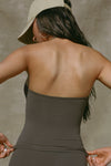 Back view of model posing in the fitted and smoothing sueded carob Halter Scoop Tank with a scoop neckline, open back and narrow, adjustable neck strap. 