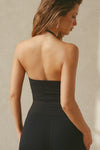 Back view of model posing in the fitted and smoothing sueded onyx Halter Scoop Tank with a scoop neckline, open back and narrow, adjustable neck strap. 