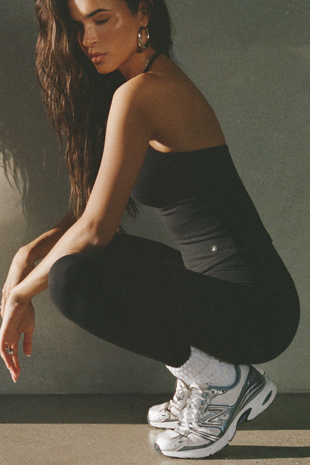 Side view of model posing in the fitted and smoothing sueded onyx Halter Scoop Tank with a scoop neckline, open back and narrow, adjustable neck strap. 