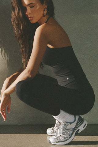 Side view of model posing in the fitted and smoothing sueded onyx Halter Scoop Tank with a scoop neckline, open back and narrow, adjustable neck strap. 