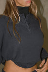 Close up detail front view of model posing in the relaxed-fit midnight luxe knit Henley Pullover long sleeve top with a buttoned henley neckline and curved hem.
