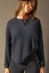 Front view of model posing in the relaxed-fit midnight luxe knit Henley Pullover long sleeve top with a buttoned henley neckline and curved hem.