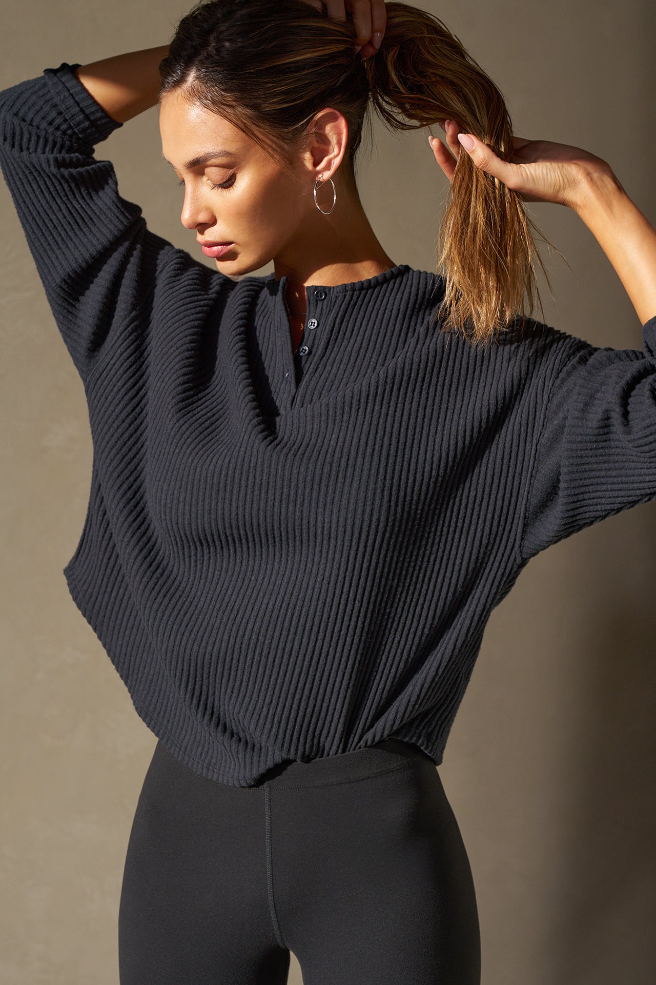 Front view of model posing in the relaxed-fit midnight luxe knit Henley Pullover long sleeve top with a buttoned henley neckline and curved hem.