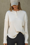 Front view of model posing in the relaxed-fit natural luxe knit Henley Pullover long sleeve top with a buttoned henley neckline and curved hem.