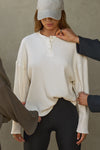 Front view of model posing in the relaxed-fit natural luxe knit Henley Pullover long sleeve top with a buttoned henley neckline and curved hem.
