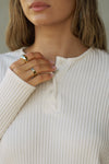 Close up detail front view of model posing in the relaxed-fit natural luxe knit Henley Pullover long sleeve top with a buttoned henley neckline and curved hem.