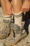 Close up side view of model adjusting the oat and olive crew Hiker Sock with ribbed detailing & two thin stripes