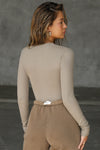Back view of model posing in the form fitting taupe flexrib Invisible Zip Long Sleeve top with a 3/4 front invisible zipper and a crew neckline