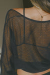 Close up back view of model posing in the sheer, relaxed fit black polka dot lace Knotted Crop Cardigan long sleeve top with an open front, and adjustable front tie that can be knotted at the center for a customizable fit and shape.