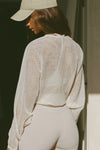 Back view of model posing in the sheer, relaxed fit cream polka dot lace Knotted Crop Cardigan long sleeve top with an open front, and adjustable front tie that can be knotted at the center for a customizable fit and shape.