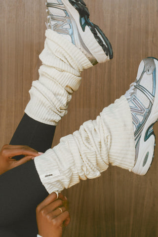 Close up side view of model adjusting the slouchy, pull on natural luxe knit Leg Warmers that can be worn pulled up on scrunched down