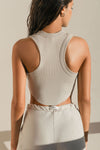 Back view of model posing in the fitted cropped dune rib Body Tank with curved hemline and a high banded crew neckline and racerback silhouette