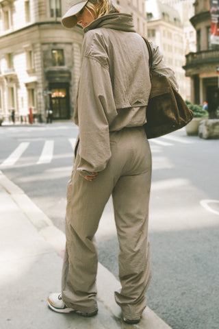 Full body back view of model posing in a city street in the relaxed fit desert sage nylon Classic Track Pant with a straight-leg silhouette, adjustable drawstring elastic waistband and side pockets 