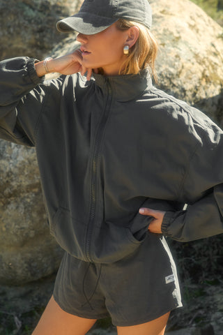 Side view of model posing outside in the relaxed-fit jet nylon Classic Track Short with an elastic waistband, side seam pockets, and adjustable drawcord.