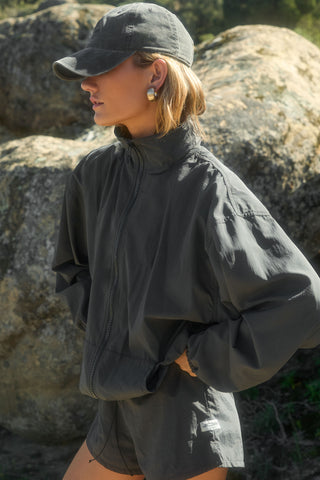 Side view of model posing outside wearing the six-panel washed black Official Cap with a curved brim and an embroidered upside down Joah Brown logo on the front