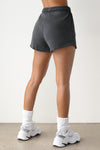 Back view of model from the waist down posing in the relaxed fit washed black french terry Sweat Short with side pockets, hidden drawstring, and an adjustable elastic waistband.