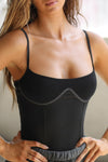 Close up front view of model posing in the fitted black flexrib Corset Tank with a low neckline, corset-style seaming at the bodice and thin, glossy elastic straps