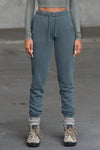 Front view of model from the waist down posing in the tapered evergreen french terry Empire Jogger with side pockets and an elastic waistband and ankle cuffs