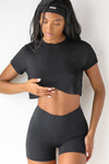 Front view of model posing in the soft cropped black modal Deconstructed Crop Tee with a crew neckline and exposed seams