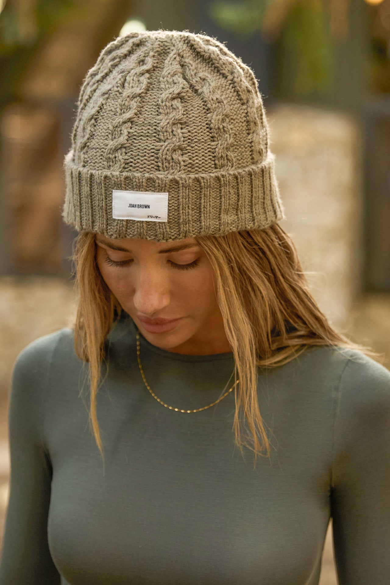 Front view of model posing outside in the soft and warm oak Cable Knit Beanie that has a custom JOAH BROWN dreamer  logo patch on the front