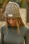 Front view of model posing outside in the soft and warm oak Cable Knit Beanie that has a custom JOAH BROWN dreamer  logo patch on the front