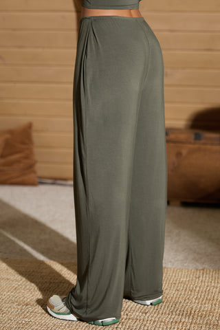 Back view of model from the waist down posing in the relaxed fit spruce modal Relaxed Straight Leg Pant with a wide leg, elastic waistband, adjustable drawstring tie and subtle pleating at the sides.