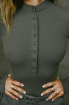 Close up detail front view of model posing in the fitted and stretchy mineral rib Button Down Henley long sleeve top with a high crew neckline and front buttons that reach about halfway down the shirt
