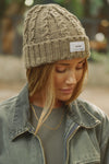 Front view of model posing outside in the soft and warm oak Cable Knit Beanie that has a custom JOAH BROWN dreamer  logo patch on the front