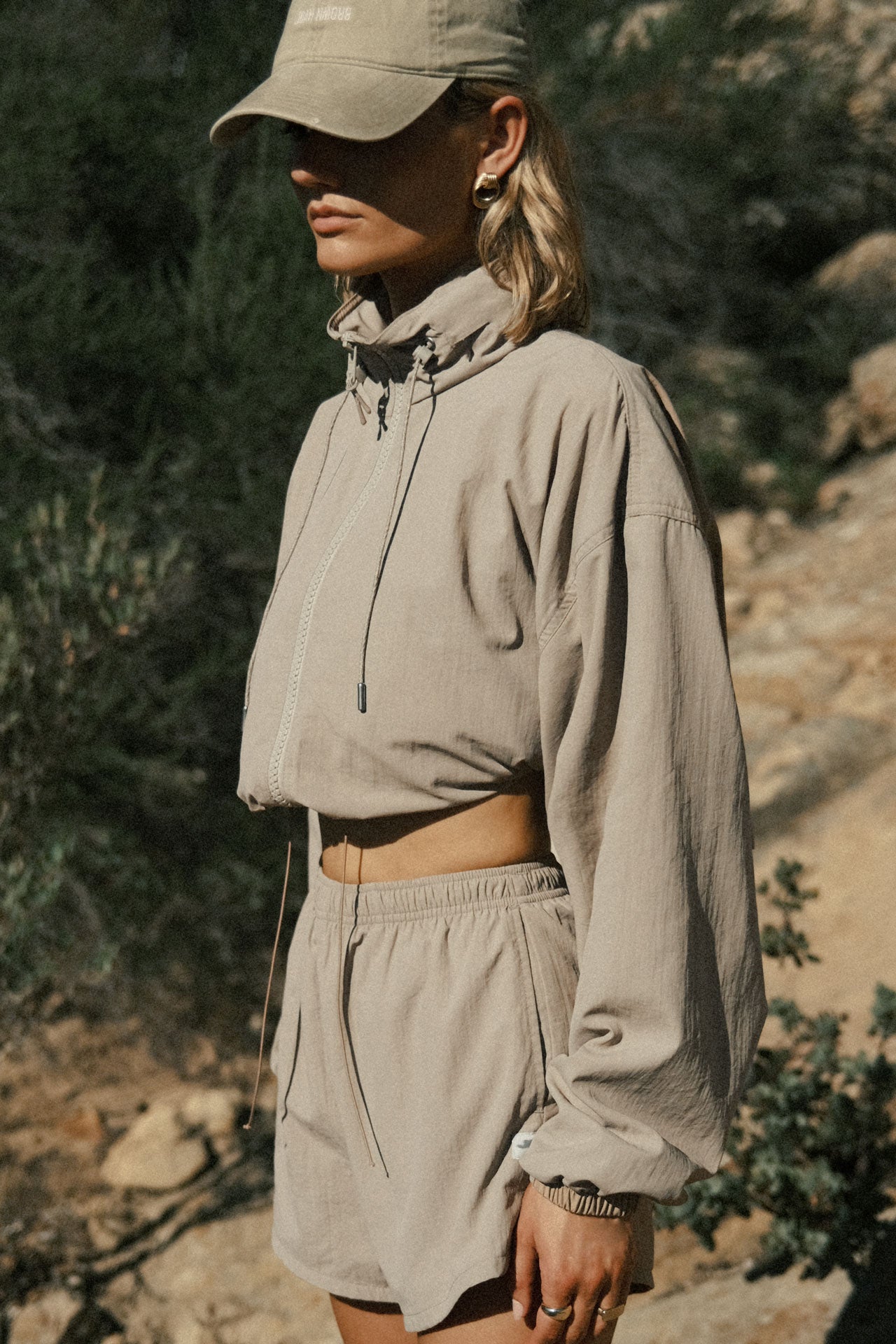 Side view of model posing outside in the relaxed-fit desert sage Classic Windbreaker Jacket with a padded collared neck for structure & adjustable corded details at the sweep for cinching