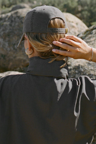Back view of model posing outside wearing the six-panel desert Official Cap with a curved brim and adjustable strap