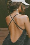 Close up back view of model posing in the fitted charcoal washed rib Cross Back Midi Dress with an asymmetrical hem, a low scoop back and thin adjustable straps that criss cross in the back