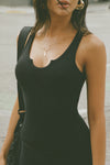 Side view of model posing in the street wearing the fitted, full length vintage black flexrib Henley Tank with a notched henley neckline