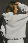 Back view of model posing in the oversized comfortable classic grey french terry Oversized Pullover Hoodie sweatshirt with paneling on the back and arms and thumbholes