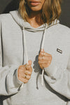Close up front view of model posing in the oversized comfortable classic grey french terry Oversized Pullover Hoodie sweatshirt with a Joah Brown logo patch at the front left chest, kangaroo pocket, drawstrings and thumbholes