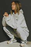 Front view of model posing in the oversized comfortable classic grey french terry Oversized Pullover Hoodie sweatshirt with a Joah Brown logo patch at the front left chest, kangaroo pocket, drawstrings and thumbholes