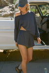 Front view of model posing next to a truck in the full-length navy modal Relaxed Long Sleeve top with dropped shoulders and a wide neckline that can be worn off the shoulders.